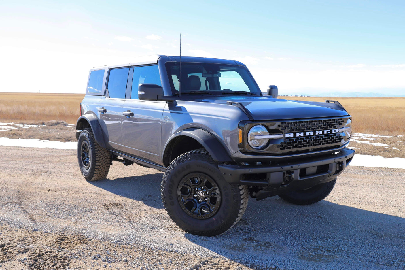 Gray Ford Bronco 4-door on a dirt road in a field, perfect for outdoor trips. An adventurous alternative to an RV rental.