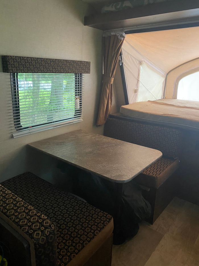 Explore this comfortable RV rental interior: dinette, window, and pop-up camper bed area.