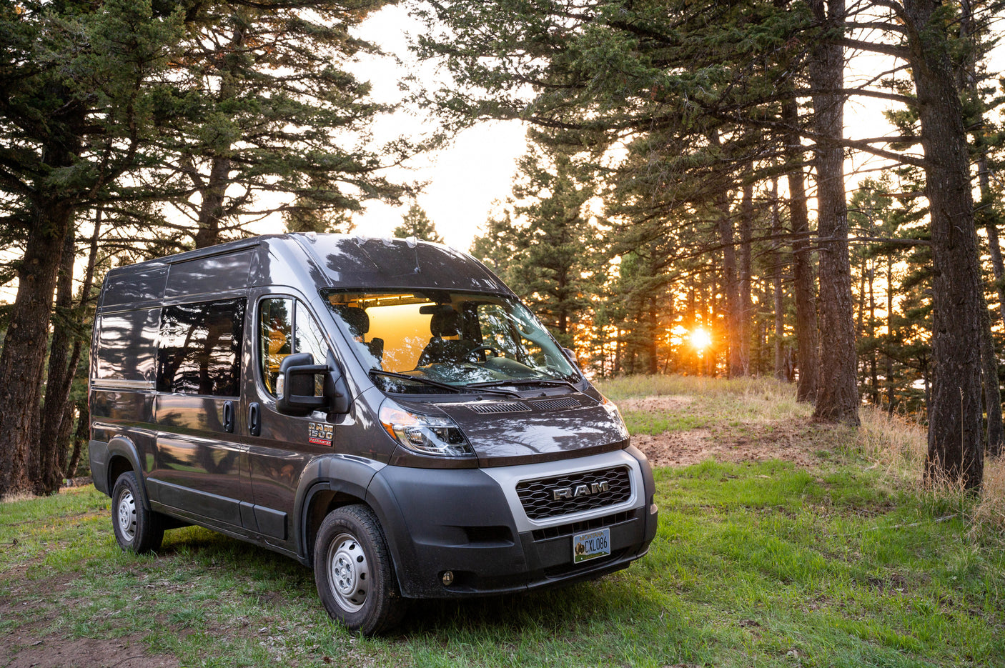 Gray Ram ProMaster campervan RV rental parked among trees with a warm sunset glow. Perfect for outdoor adventure.