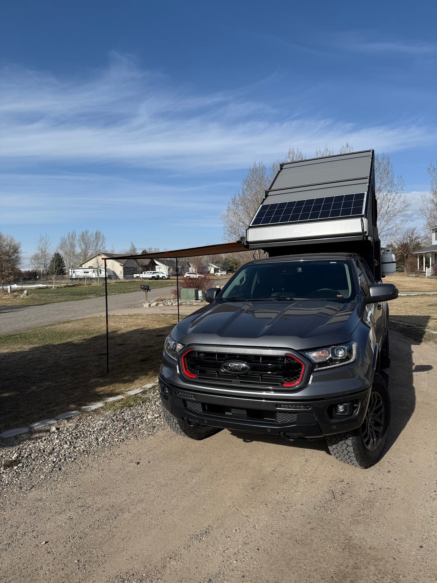 This grey Ford truck features an RV rental-style pop-up camper with solar panels and an awning, ready for overlanding.