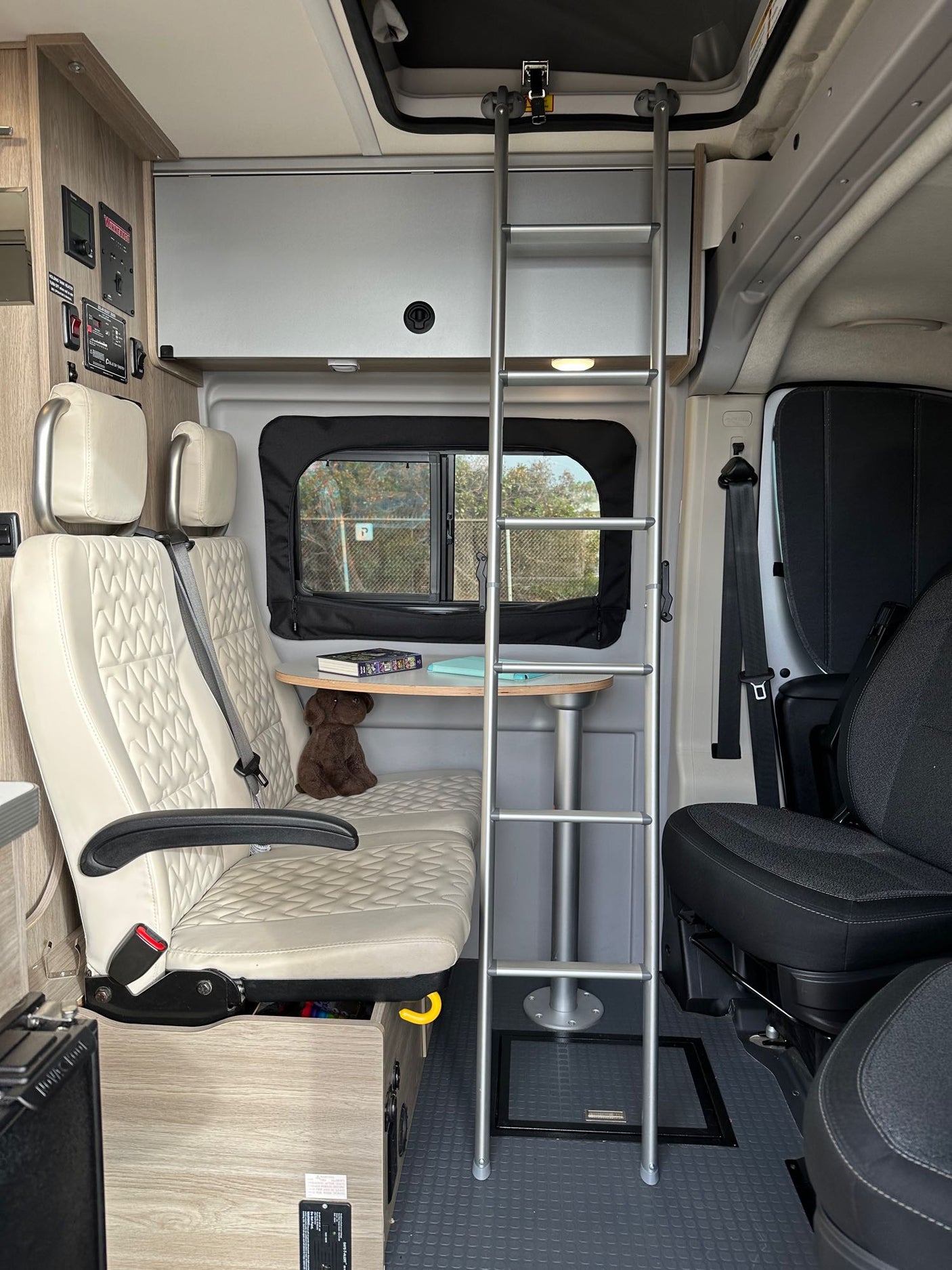 Cozy RV rental interior: dinette with table, seats, ladder to bed, and control panel visible.