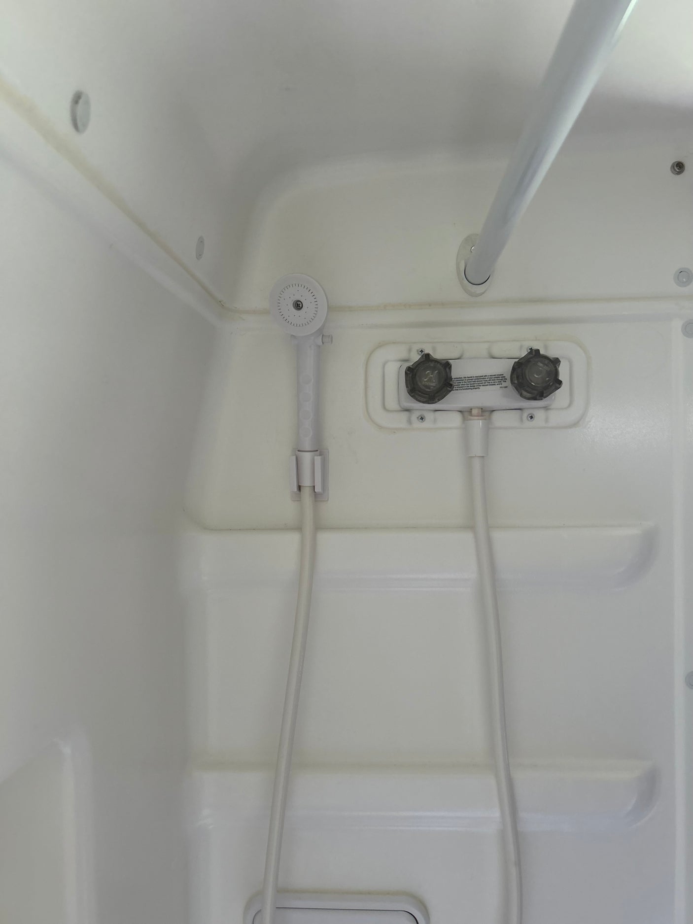 Compact white shower in an RV rental, with a hand-held shower head, faucet controls, and a grab bar.
