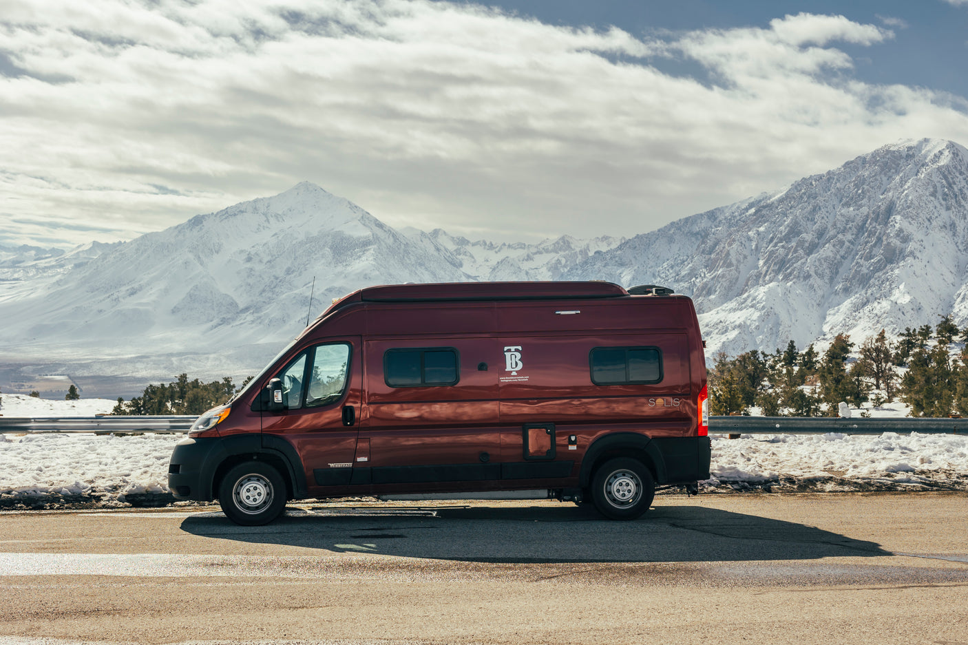 Red Winnebago Solis RV rental parked against a backdrop of majestic snow-covered mountains. Ideal for scenic road trips.