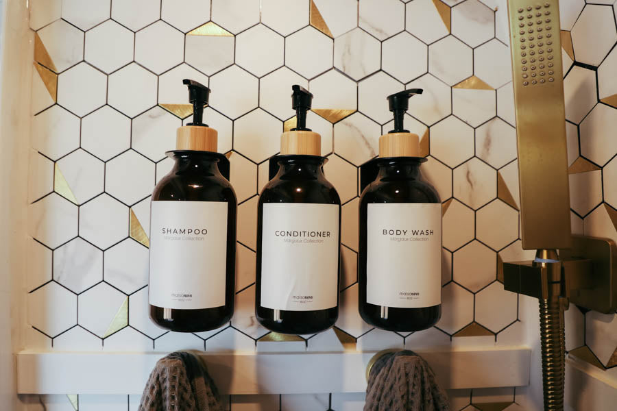 RV rental bathroom features organized shampoo, conditioner, body wash bottles, gold shower, hexagon tiles, & towels.