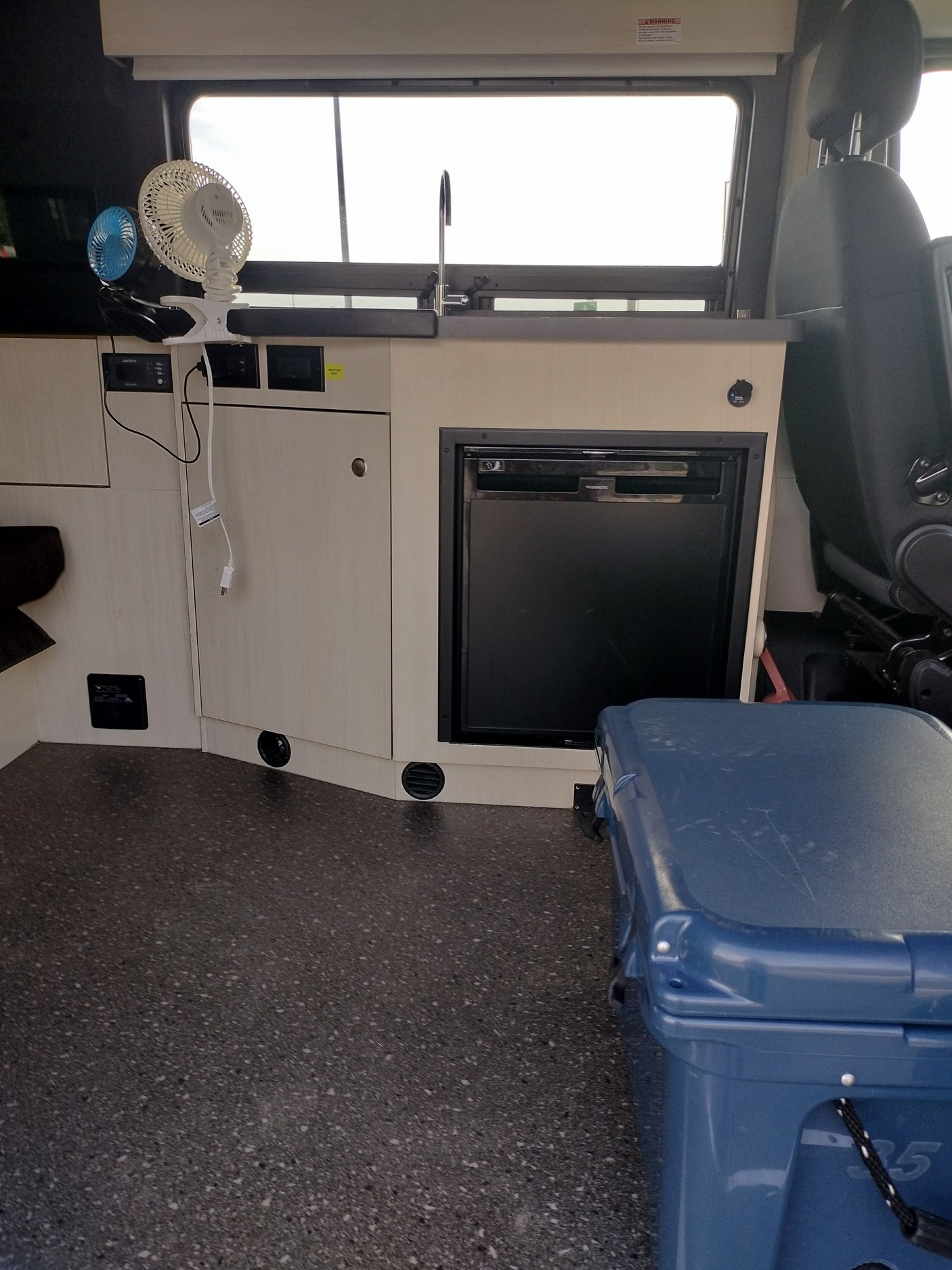 Inside this rv rental, a compact kitchen features a sink, refrigerator, and handy fans. A large cooler sits on the floor.