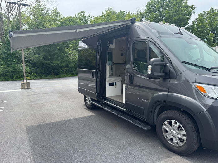 Explore comfort with this grey RV rental camper van, side door open and awning extended. Ready for your next road trip!