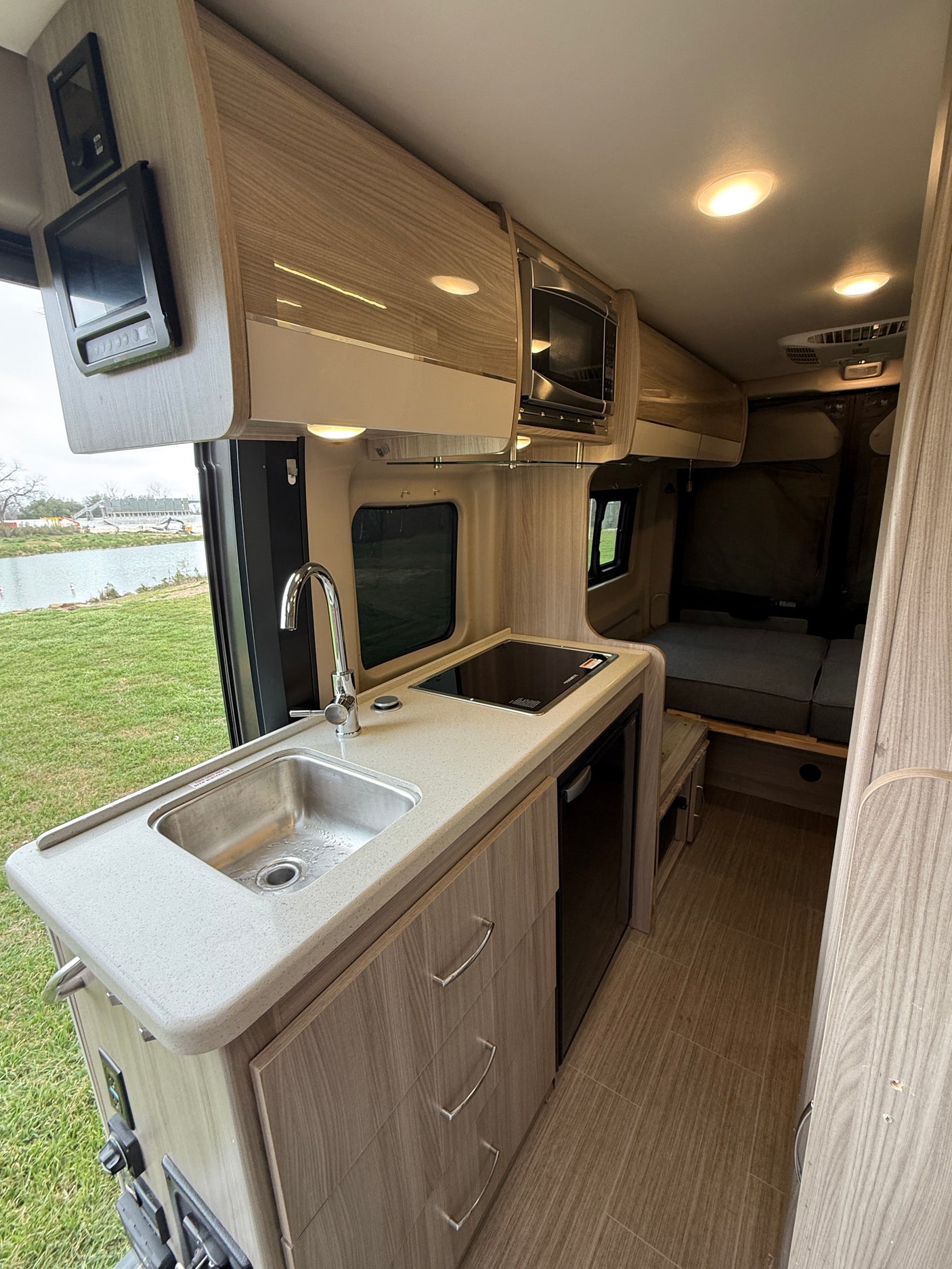 Inside a modern RV rental: well-equipped kitchenette with sink, stovetop, microwave, and cozy rear bed area.