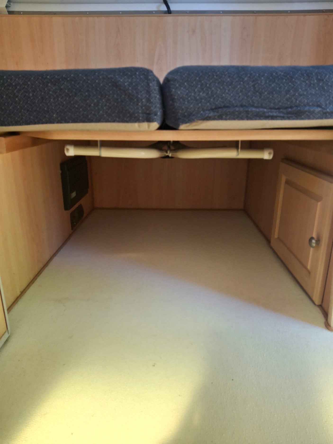RV rental interior: cozy sleeping area with storage, featuring light wood, dark cushions & a small cabinet.