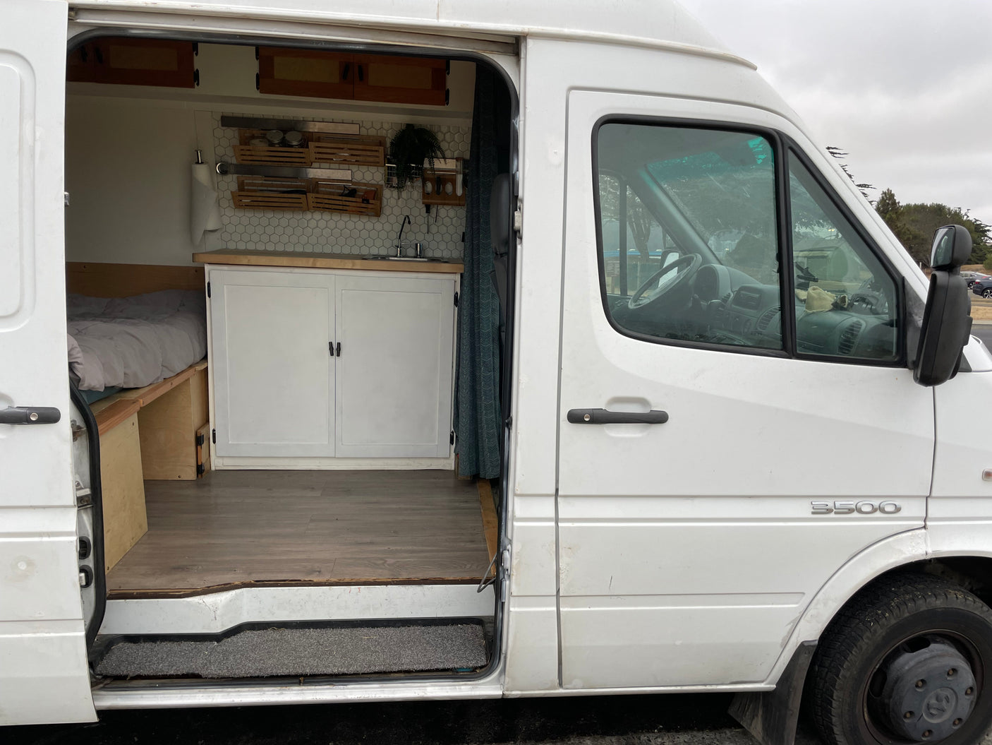 White Sprinter camper van for RV rental, showing interior kitchenette, bed, and driver's area.