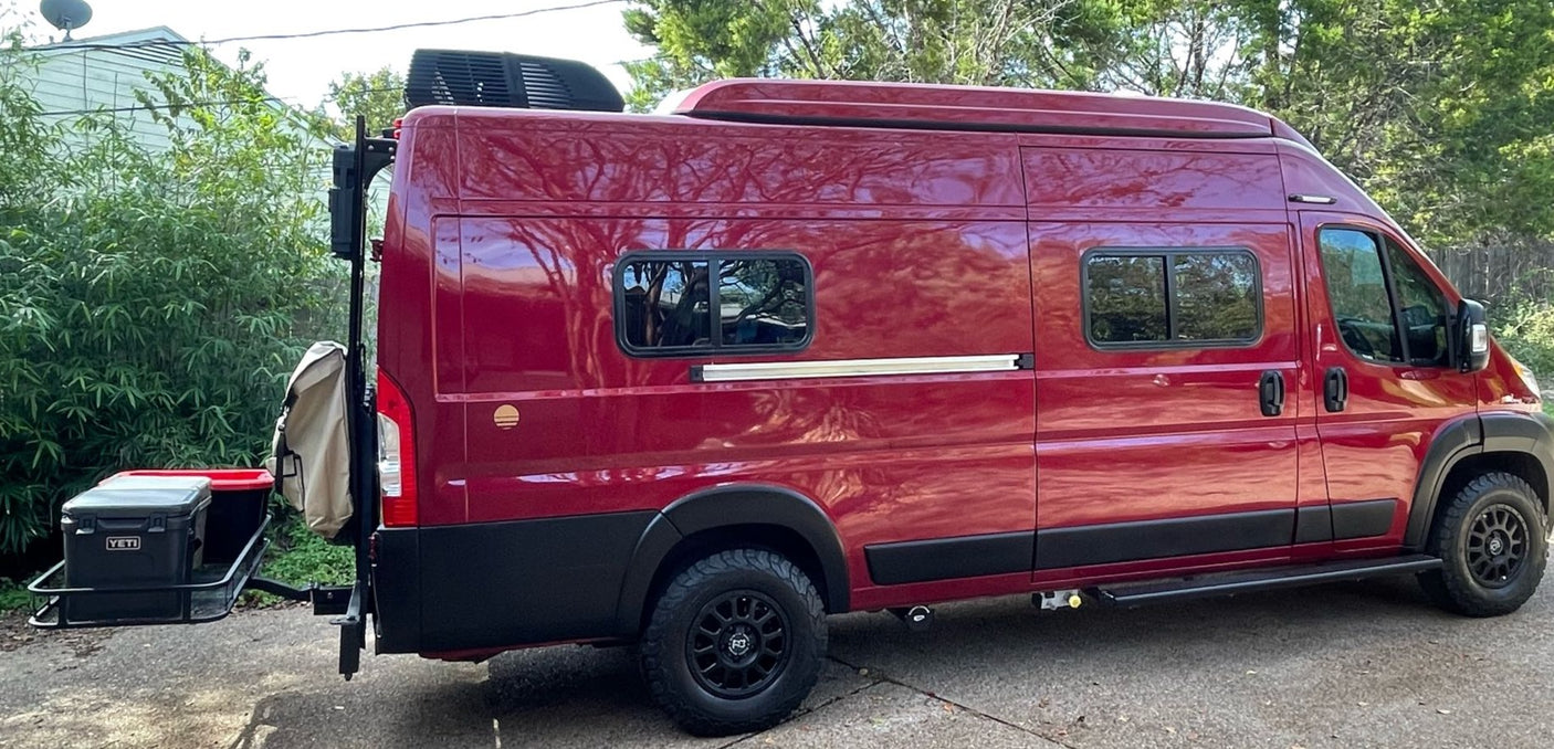 Explore in this custom red camper van, available for RV rental. Features a roof AC and rear cargo carrier with a Yeti cooler.
