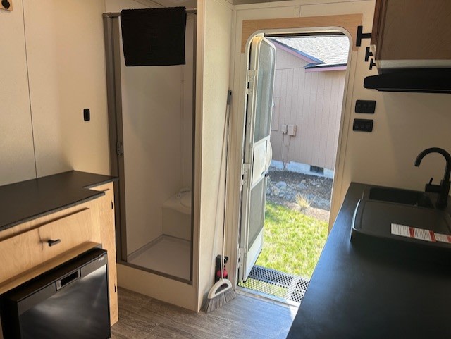 and a kitchenette with light wood cabinets and dark counters.|RV rental's compact kitchen: light wood cabinets