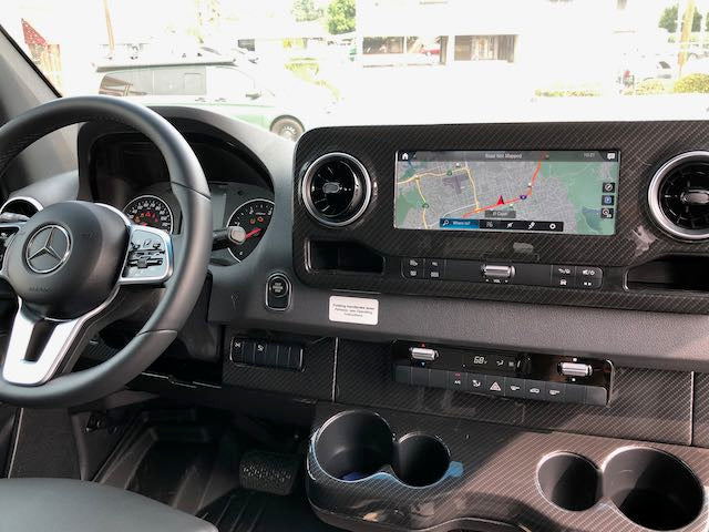 View of a modern Mercedes RV rental interior dashboard, featuring a navigation screen, steering wheel, and climate controls.