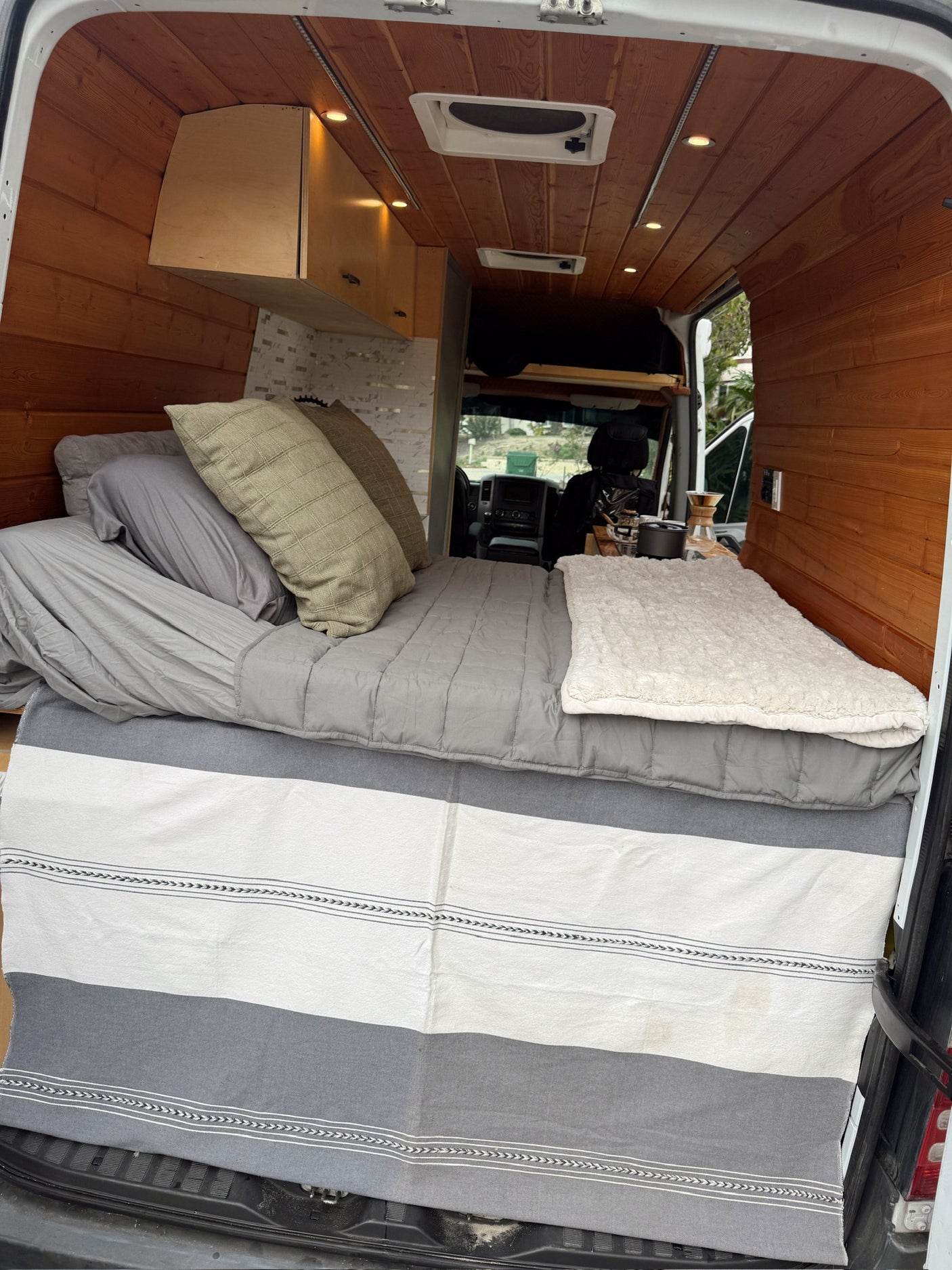 Cozy rv rental campervan interior featuring a comfortable bed, warm wood paneling, and a convenient coffee setup.