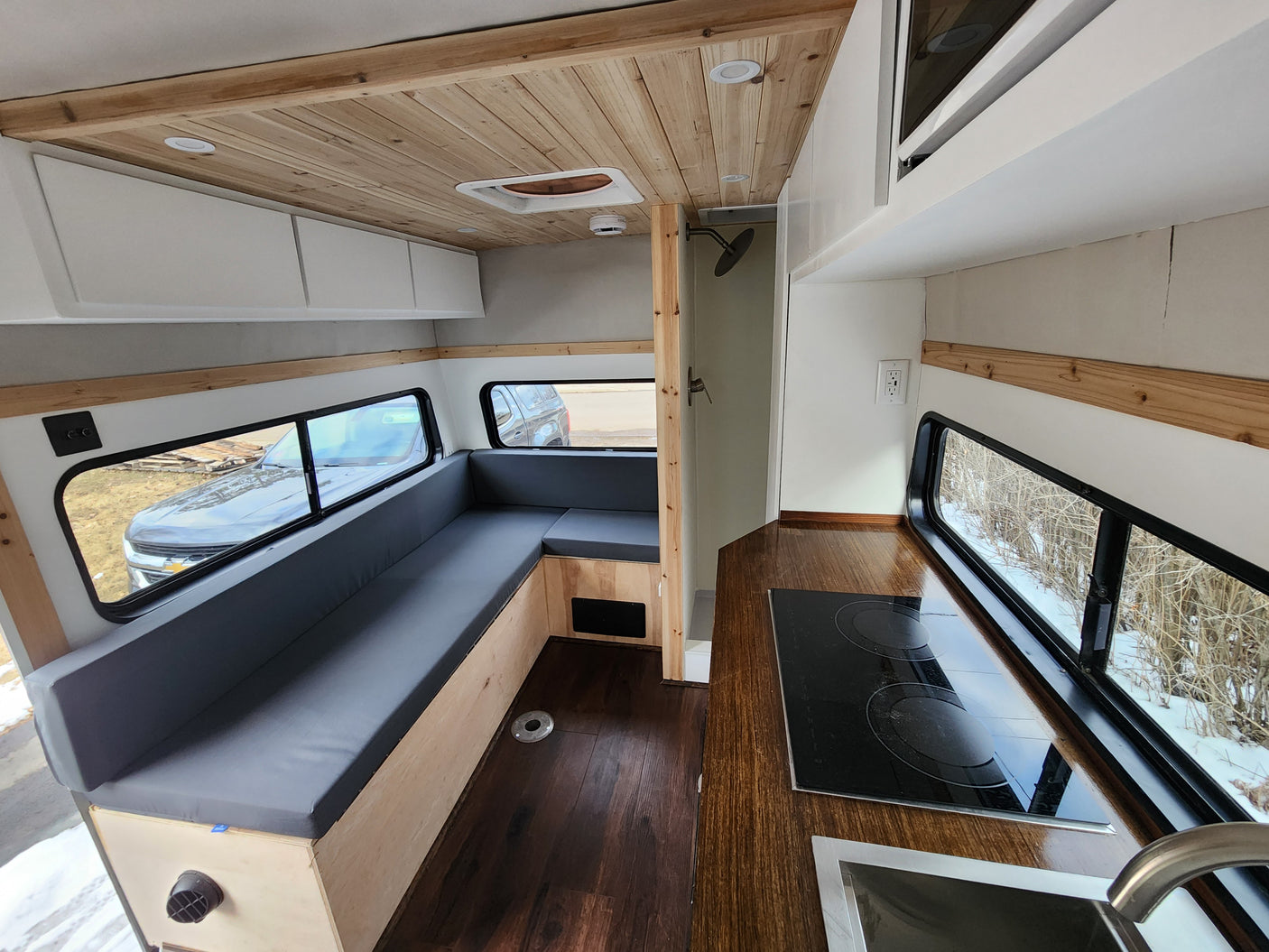 Spacious rv rental interior showing a kitchen, L-shaped seating, and shower stall, with wood and white accents.
