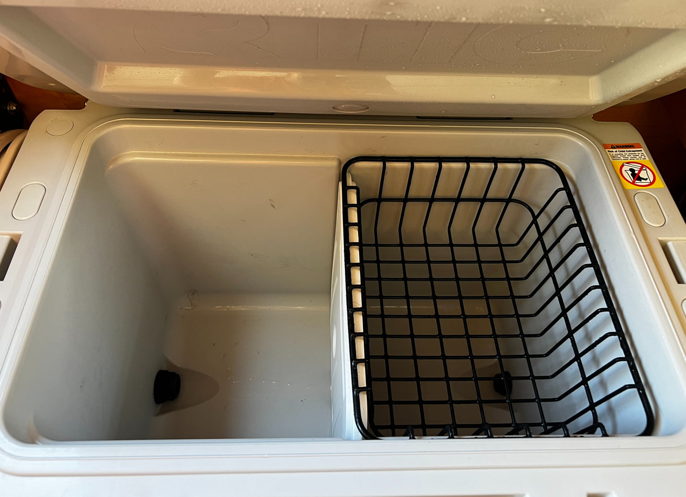 RV rental fridge interior: partitioned space with drain plug and wire storage basket for organized travel.