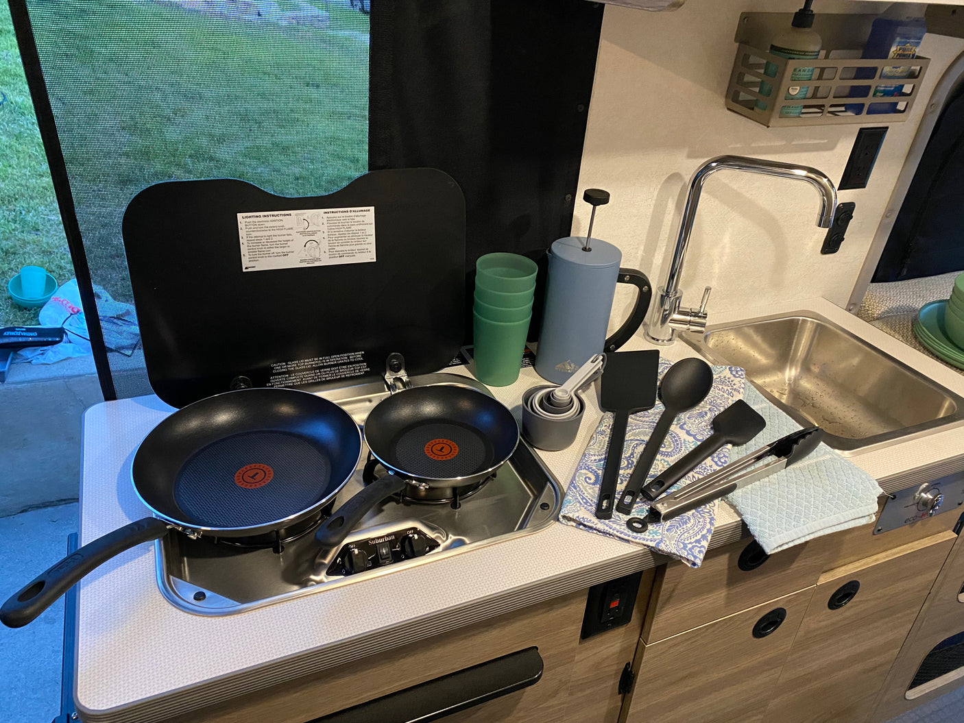RV rental kitchen setup: non-stick pans on a stovetop, a sink, French press, cups, and cooking utensils ready for use.