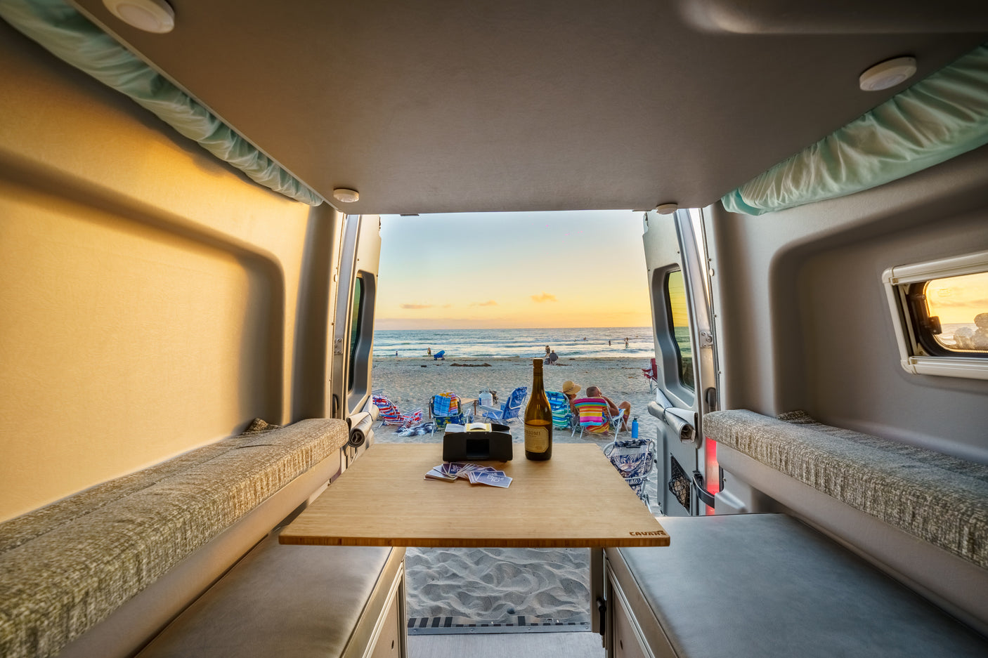 Perfect RV rental evening: beach sunset from inside a cozy camper van, with wine, cards, and ocean views.