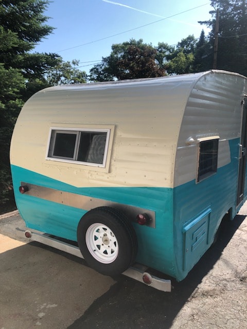 Explore with this charming vintage RV rental! Teal & cream camper with rear spare tire, ready for adventure.