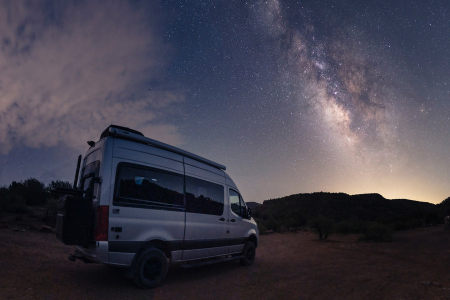 Stargazing from an RV rental: a silver van under the stunning Milky Way galaxy at night. Perfect for adventure.