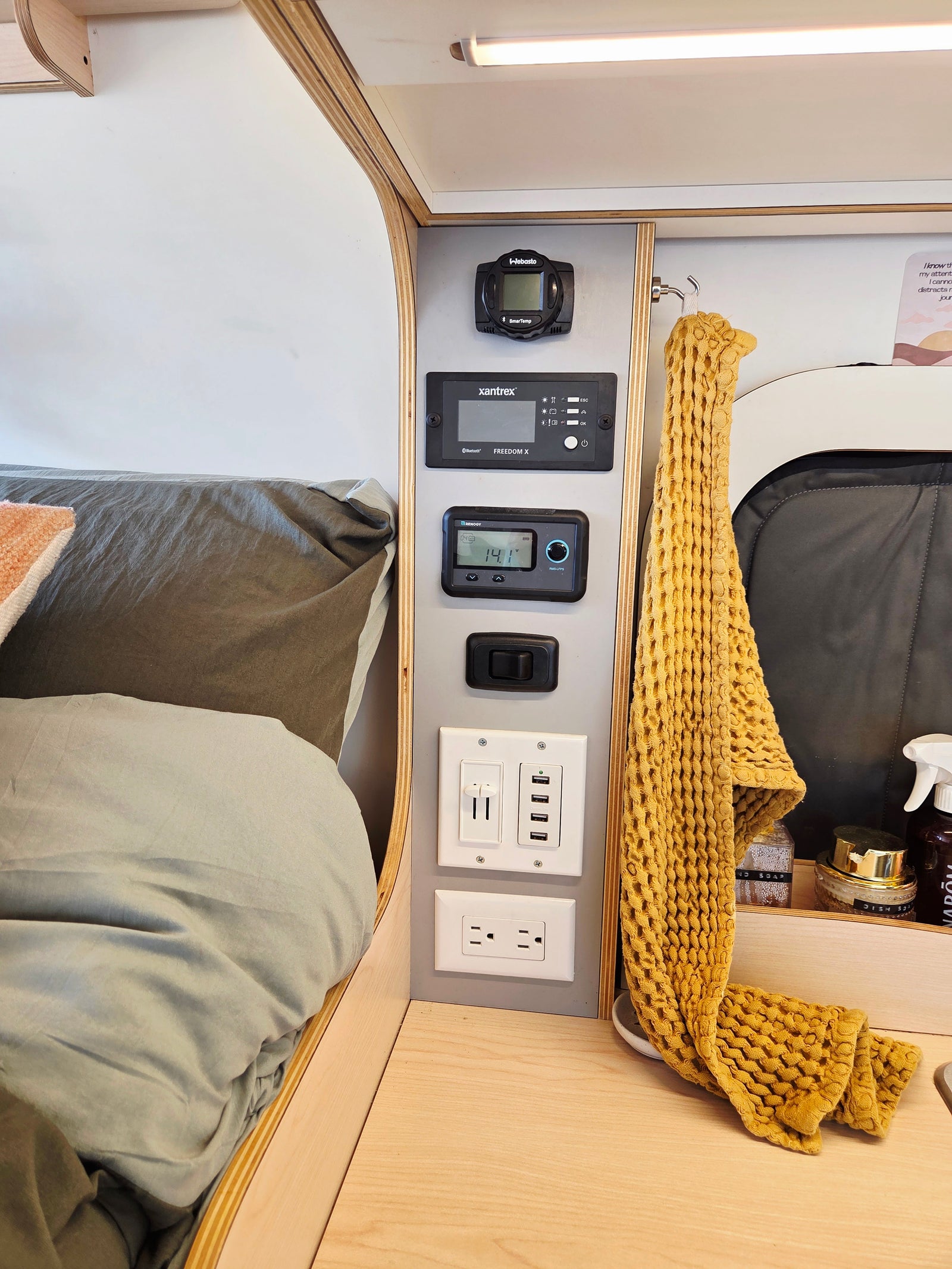 RV rental interior: bed, a multi-function control panel showing Webasto, Xantrex, Renogy, and various USB/AC charging ports.