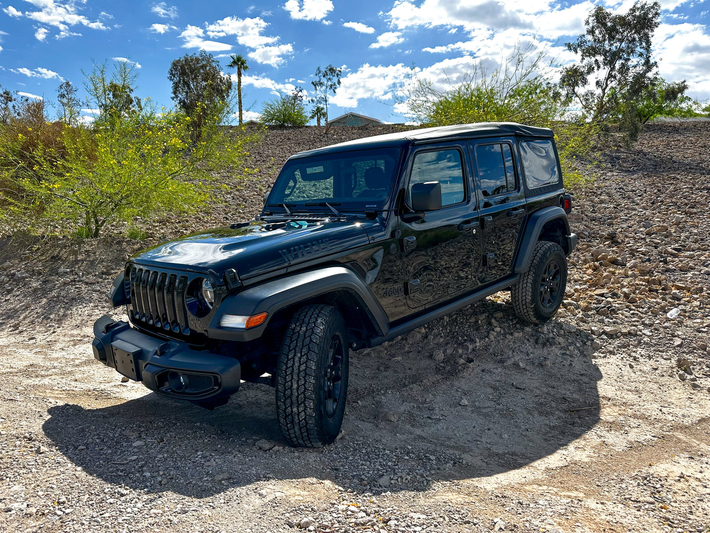 Black Jeep Wrangler on a rocky desert trail under a bright blue sky. Perfect for off-road adventures complementing your rv rental trip.