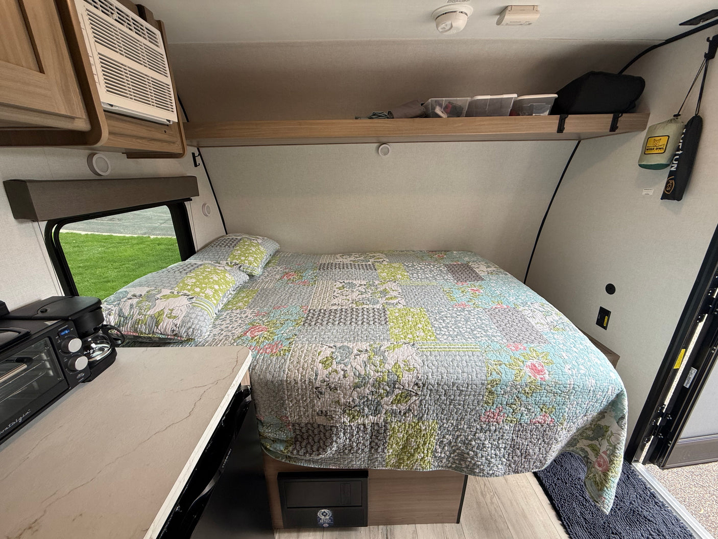 Cozy RV rental bedroom with a patchwork quilt, compact appliances, and an AC unit for comfortable travel.