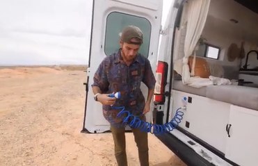 with open rear doors showcasing its cozy seating/bed and storage.|RV rental: Rear view inside a white camper van conversion with a gray cushioned bed