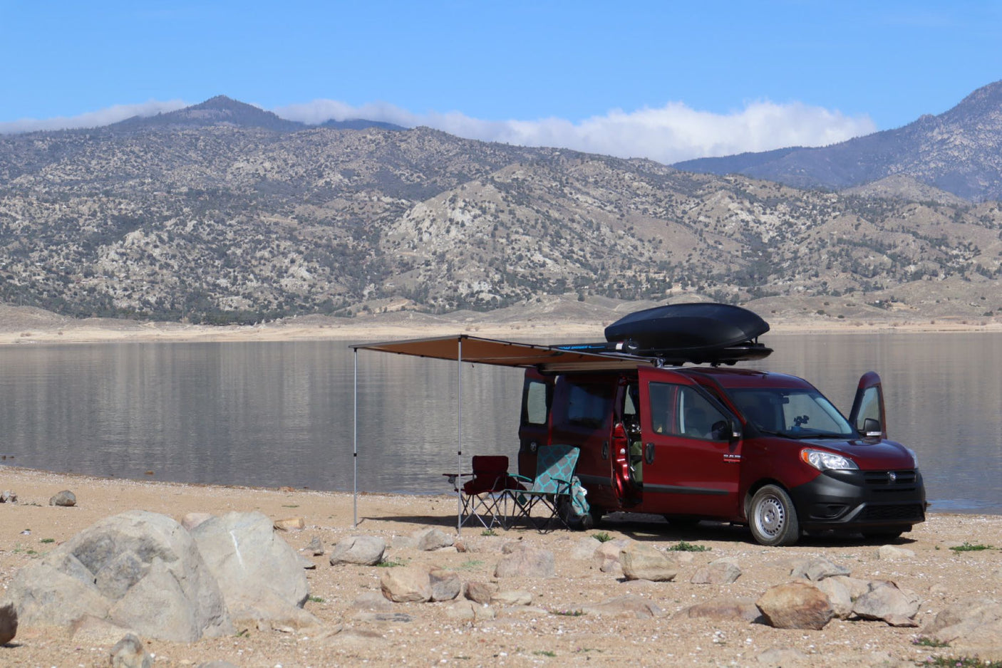 Red RV rental van camping by a lake with mountains