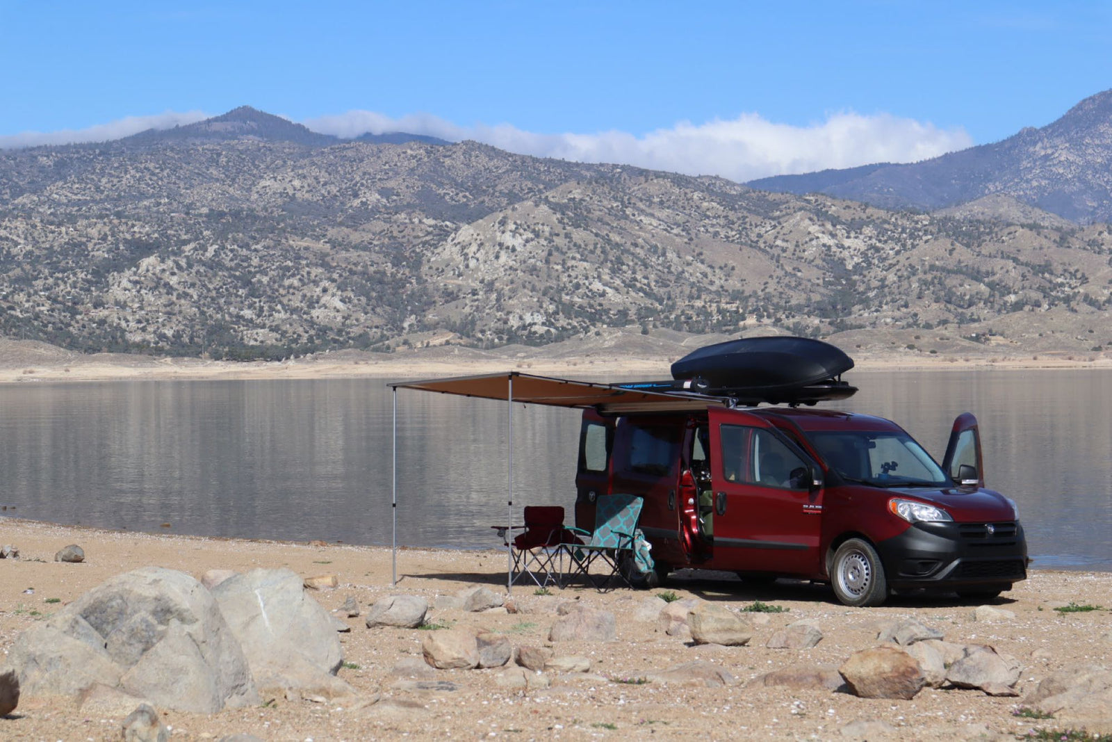 Red RV rental van camping by a lake with mountains
