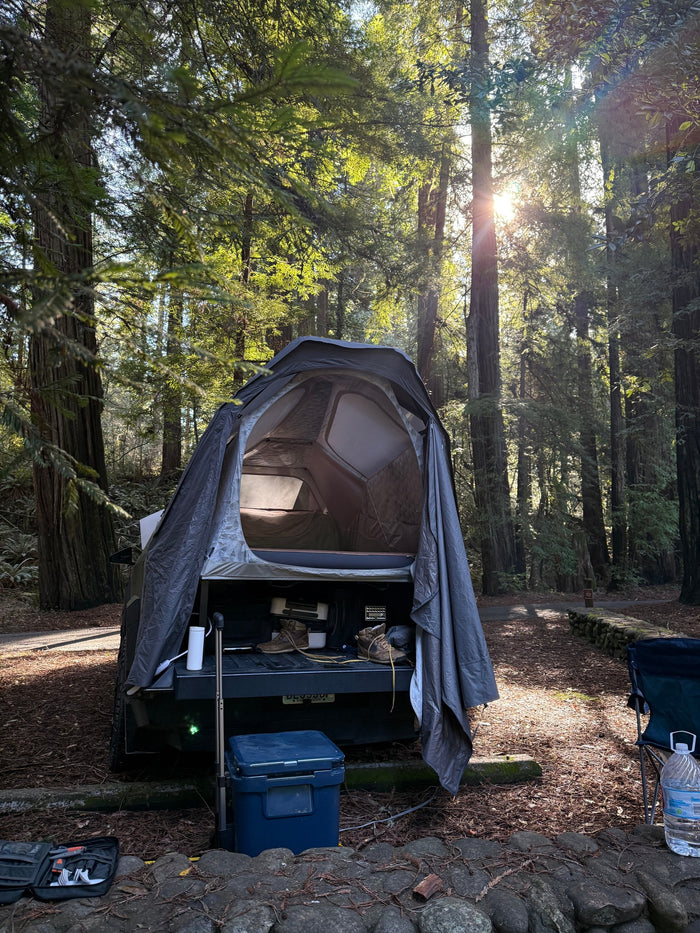 Truck bed tent camping setup in a sunlit forest, offering an adaptable RV rental alternative for adventures.