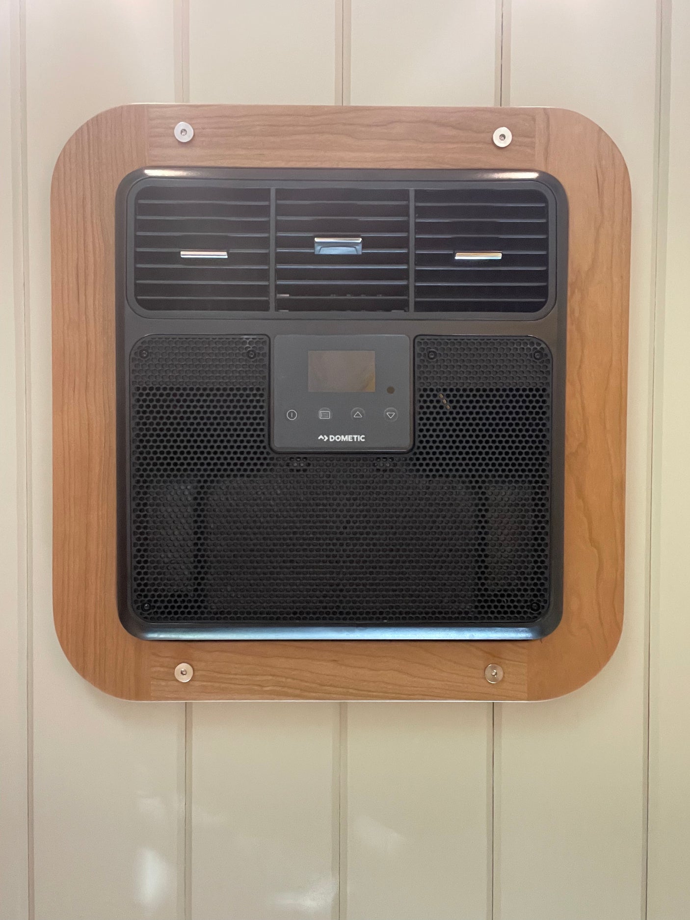 Interior of an RV rental: a Dometic air conditioner unit, with a black grille, control panel, and decorative wood frame.