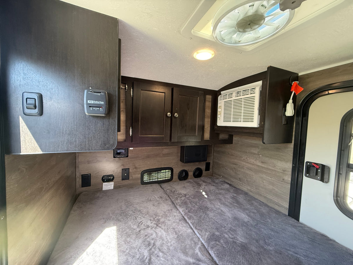 RV rental interior: a compact sleeping area with dark wood cabinets, AC, and a Suburban thermostat. — photo 4
