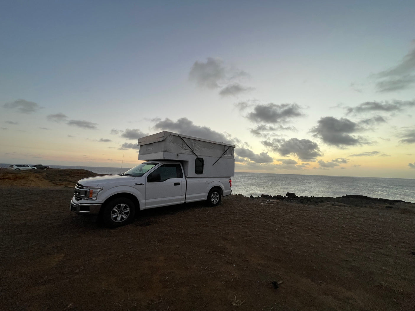 White Ford F-150 rv rental pop-up truck camper at dusk by the ocean, ideal for camping adventures.