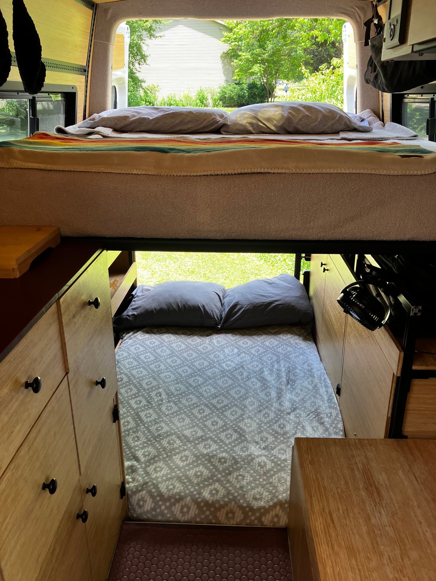 RV rental interior shows cozy bunk beds & wood cabinets, with a view of nature outside.