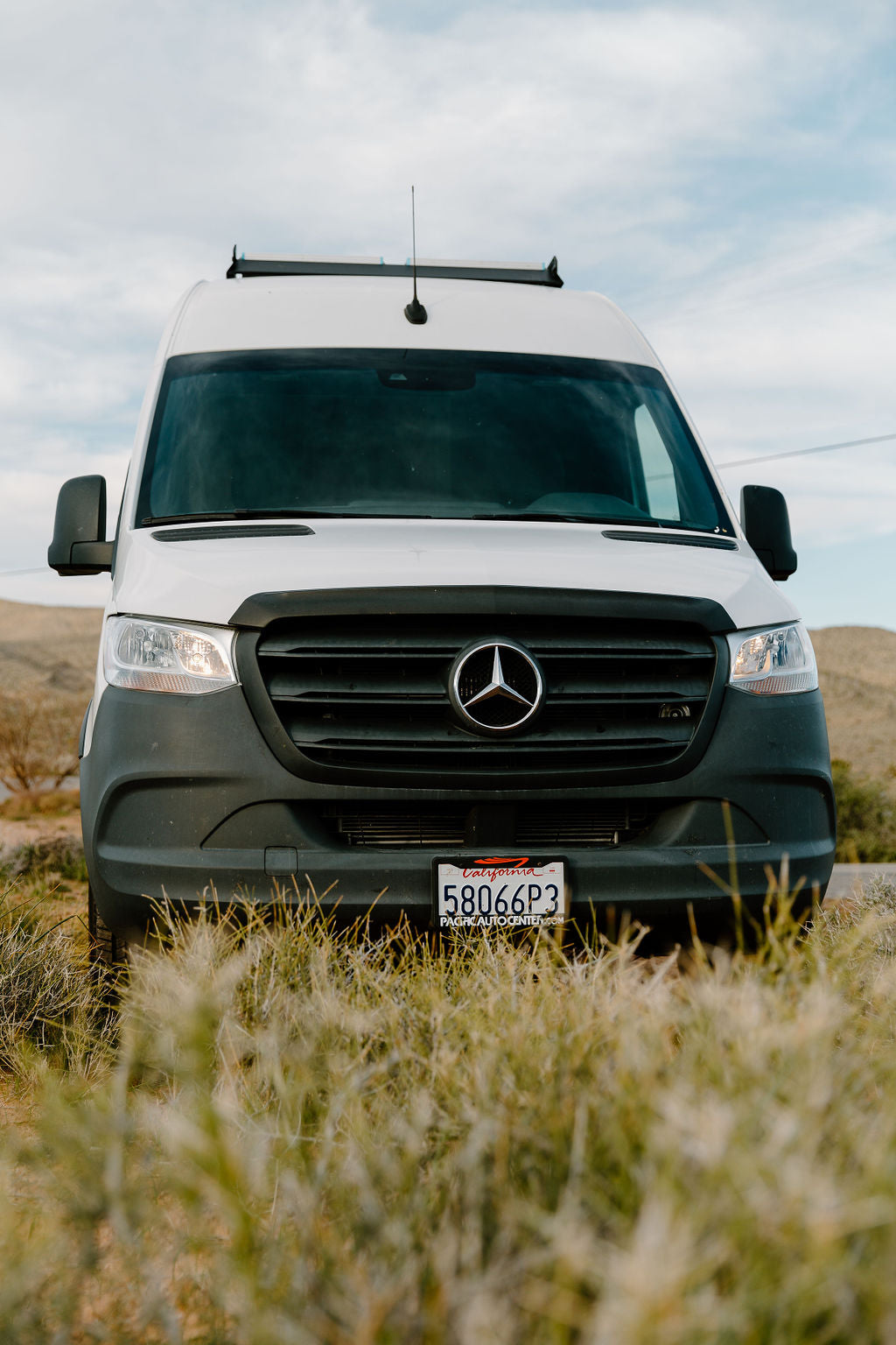 Front view of a white Mercedes Sprinter van, common as an RV rental, parked in an outdoor setting. CA plate 58066P3.