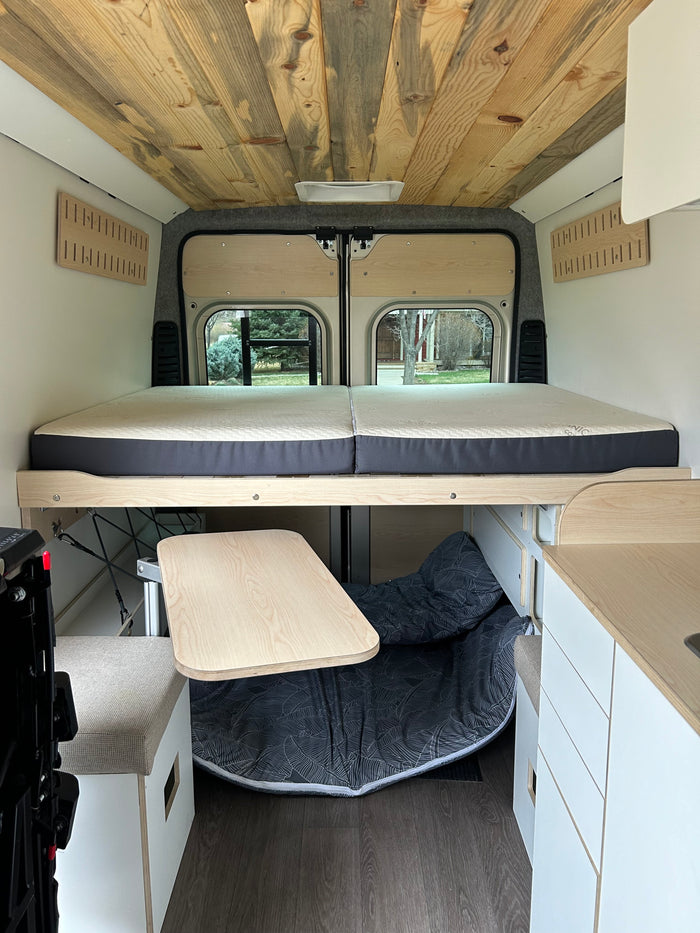 RV rental interior featuring a wooden ceiling, raised bed, and a convertible living space with a table and storage.