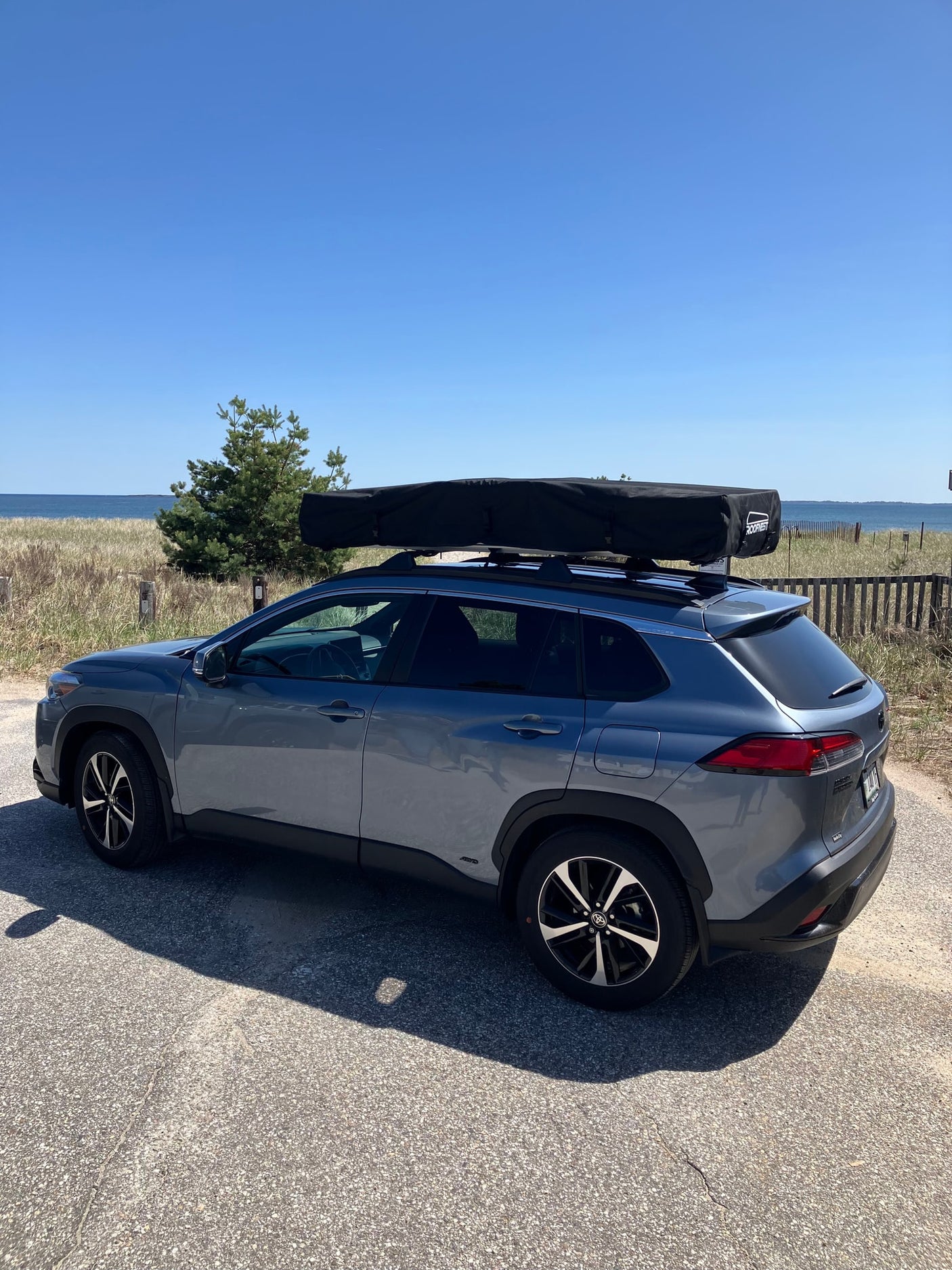 Grey SUV with a Roofnest roof tent parked by the beach, an ideal setup for a compact outdoor adventure like an RV rental.