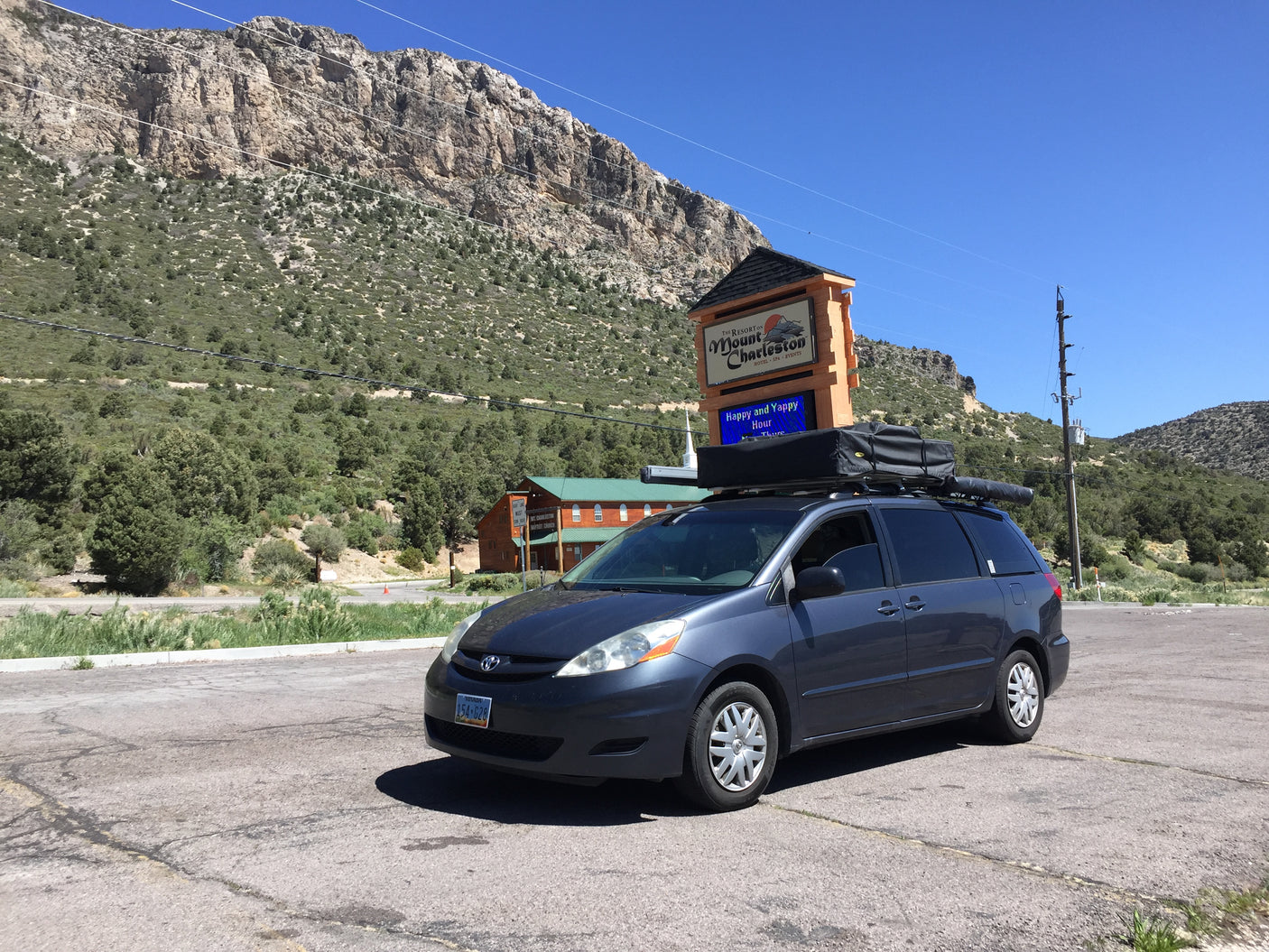 Ready for adventure! A minivan with a rooftop tent, like an RV rental, parked at Mount Charleston Resort, Nevada, with mountains.