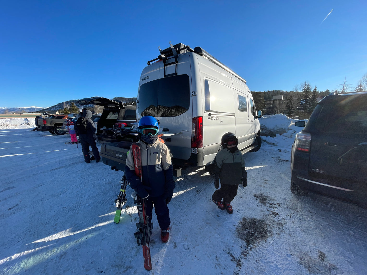 Ski day with an RV rental! Kids in winter gear in a snowy mountain parking lot. Ready for outdoor adventure.