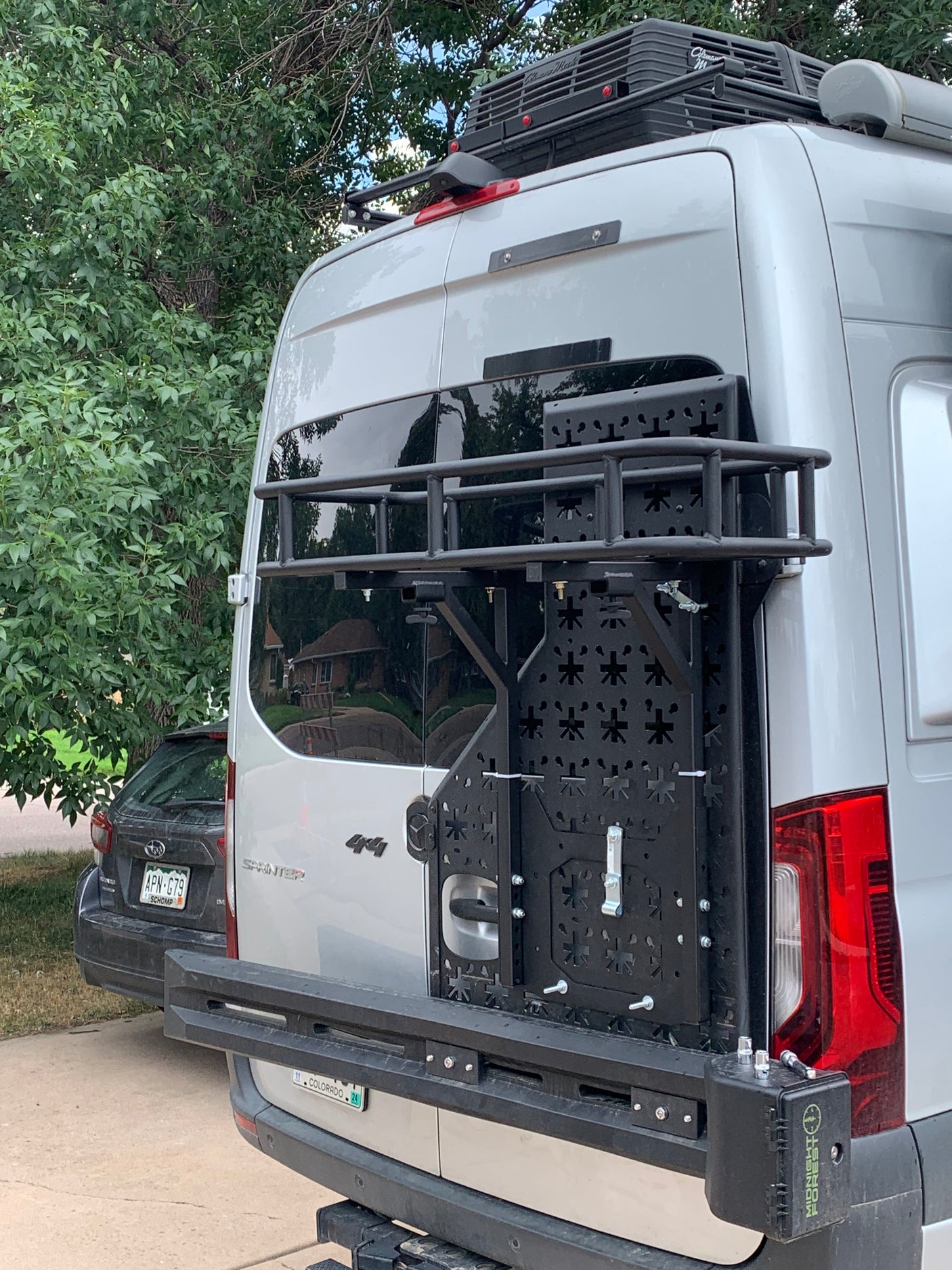 Rear of a silver Sprinter 4x4 camper van, ready for RV rental adventures with a custom cargo rack and roof AC.