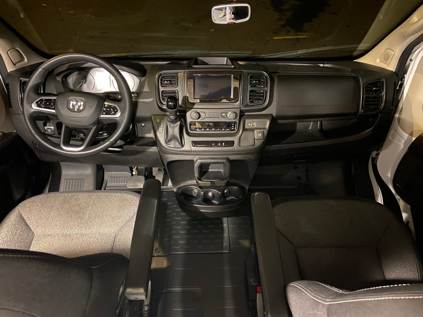 RV rental van's driver cockpit: modern dashboard, steering wheel, infotainment screen, gear shift, and front seats.