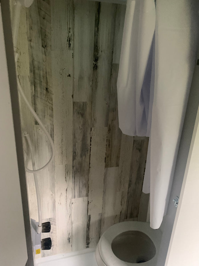 RV rental: Compact wet bath with toilet, shower hose, and white curtain against rustic wood-look walls.