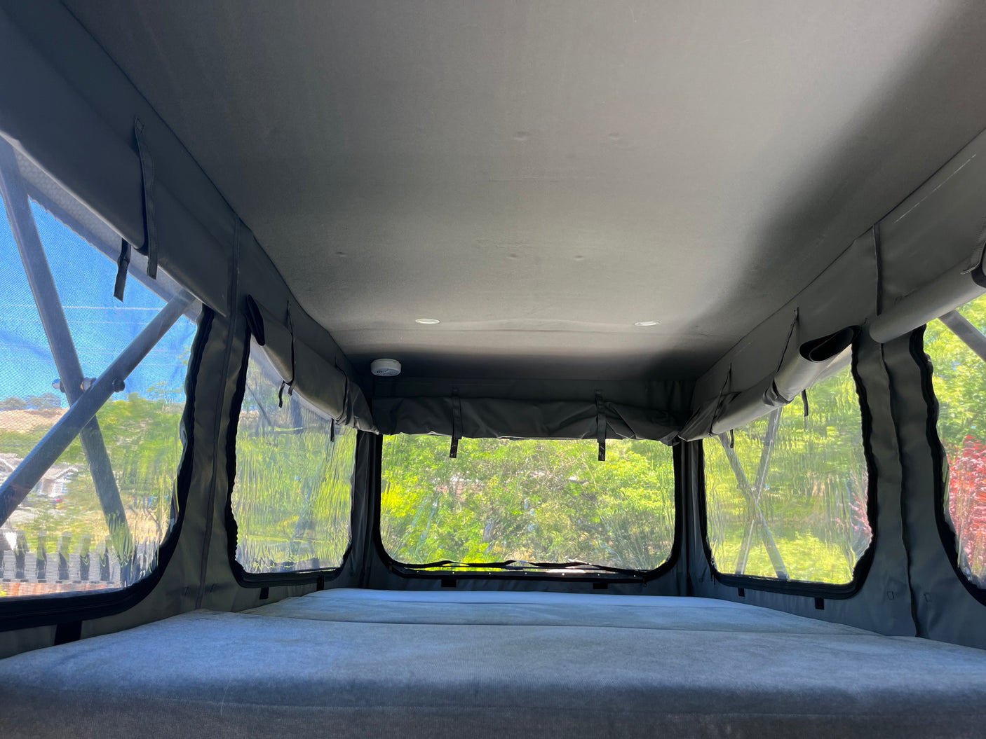 Interior of an RV rental pop-top camper with bed, clear windows looking out to nature. Includes smoke detector.