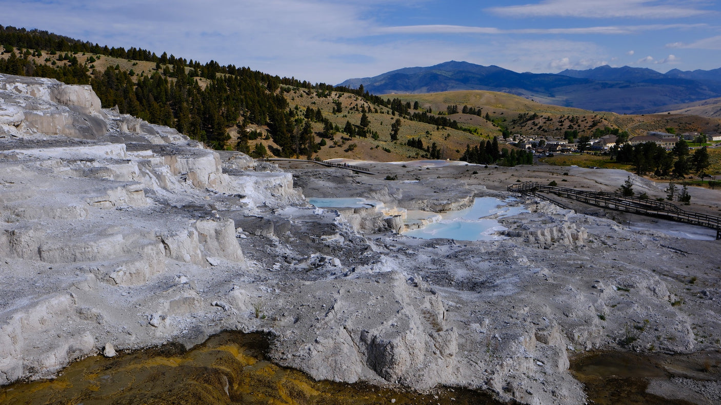 a large stone gateway with mountains behind.|Explore Yellowstone's Mammoth Hot Springs terraces from your RV rental. Boardwalks guide visitors past colorful
