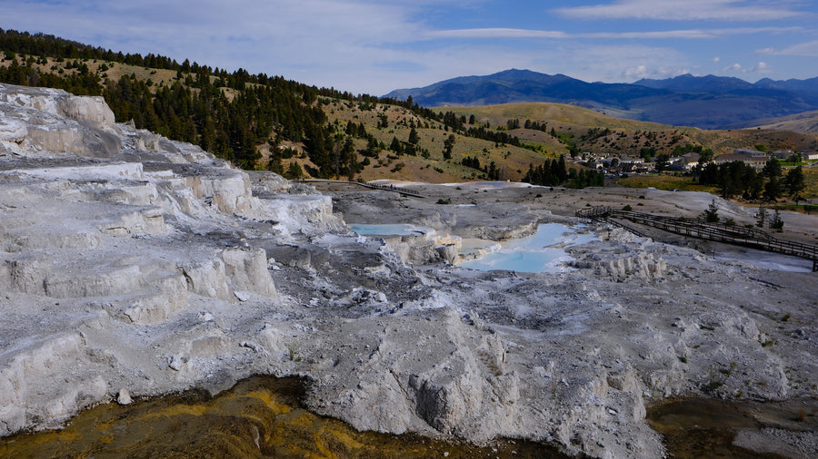 a large stone gateway with mountains behind.|Explore Yellowstone's Mammoth Hot Springs terraces from your RV rental. Boardwalks guide visitors past colorful