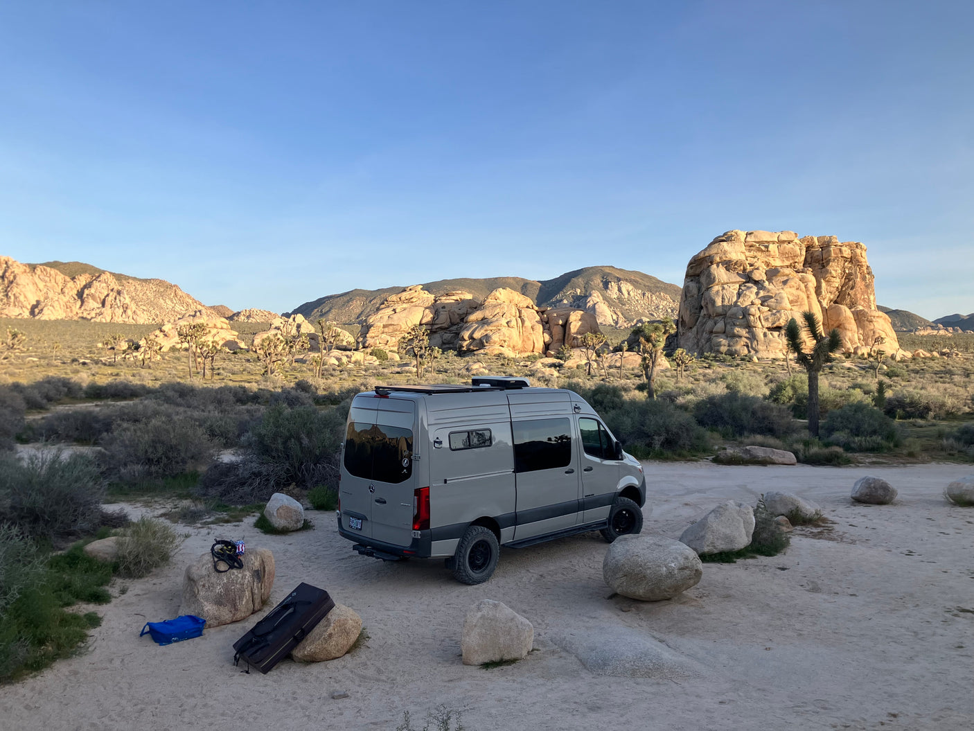 RV rental camper van parked among iconic Joshua Trees and rock formations, ready for desert adventures.