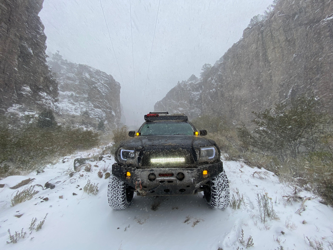 Black truck navigates a snowy canyon trail during winter. A rugged off-road adventure unlike an RV rental.