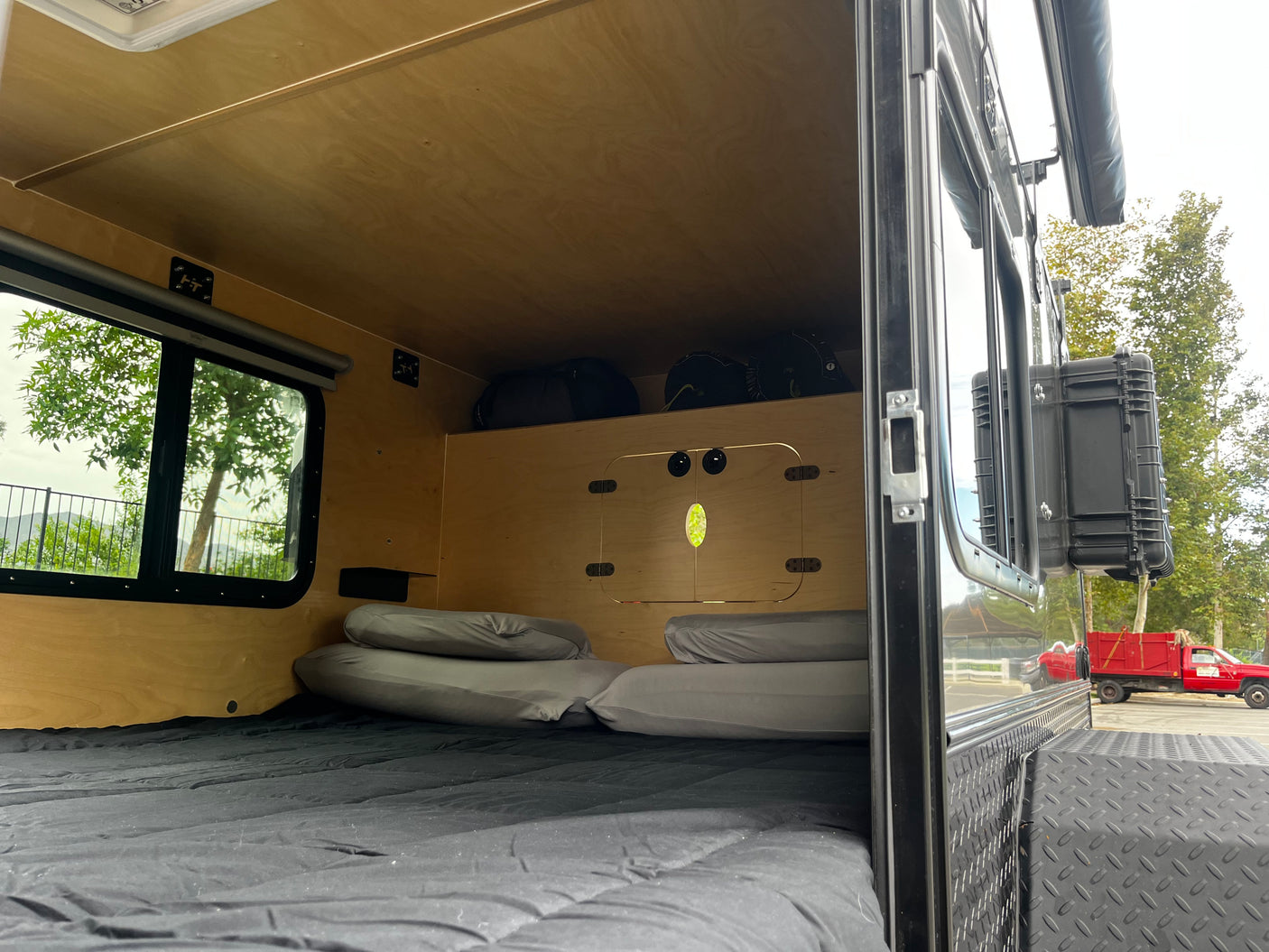 RV rental interior featuring a cozy bed, overhead storage, and a window offering a scenic outdoor view.