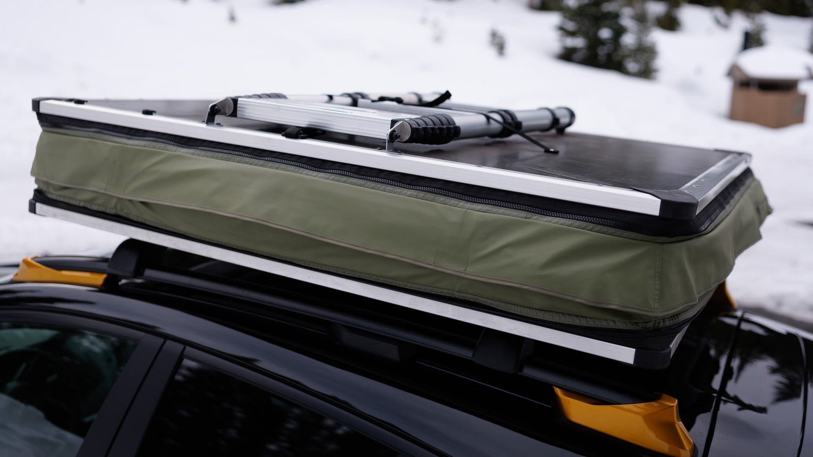 Car-top tent packed for an rv rental outdoor adventure. Ready for winter travel & camping on a snowy road.