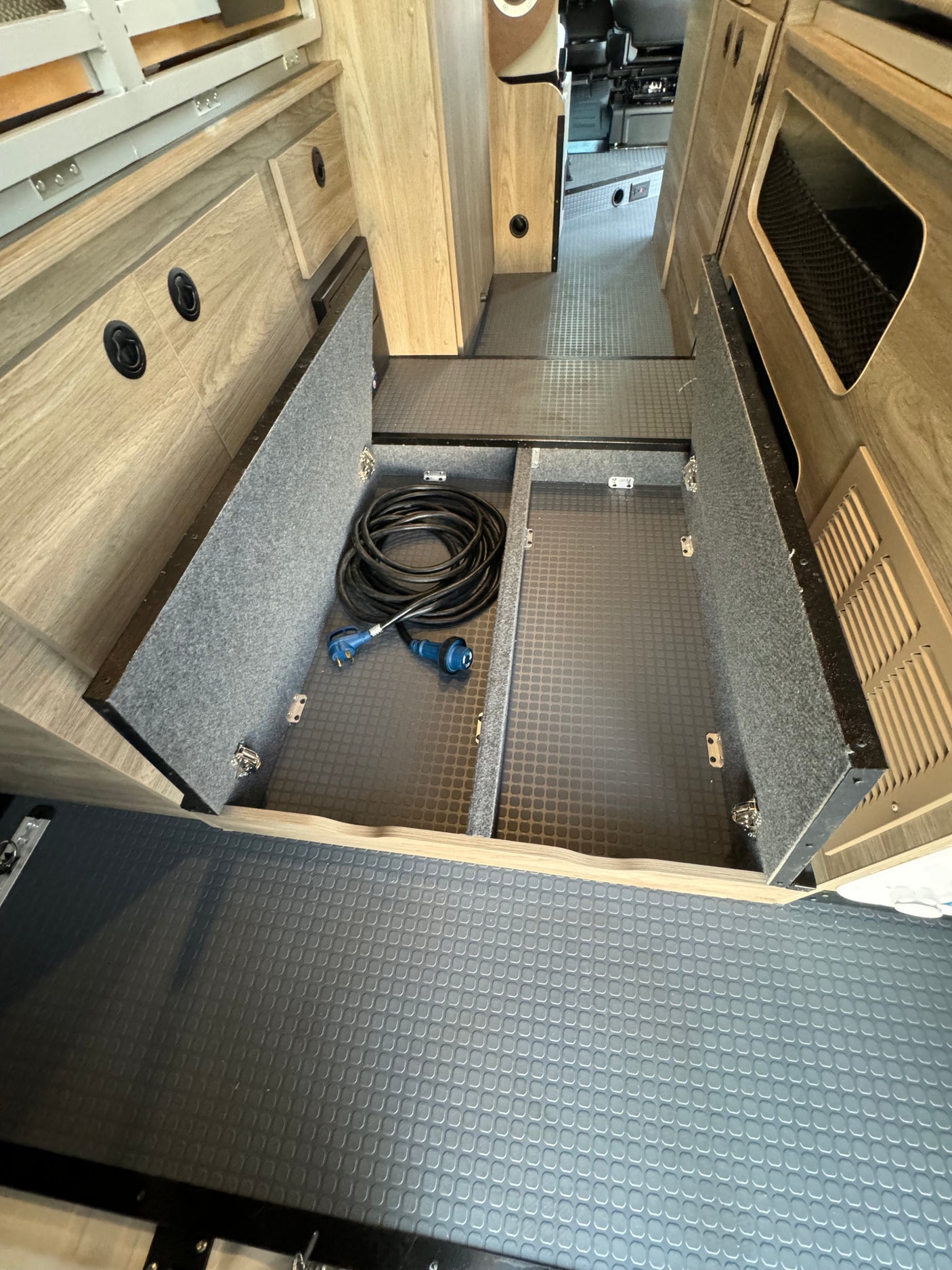 RV rental: Spacious interior showing textured floor, convenient under-floor storage with electrical cord for camping trips.